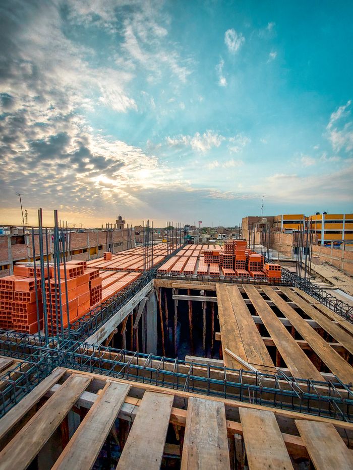 Bird's-eye view of an industrial construction site with stacks of red bricks and wooden planks under a blue sky at sunrise.